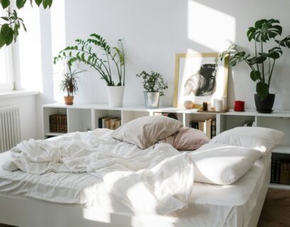 Bedroom interior with a woman arranging potted plants on shelves above a bed