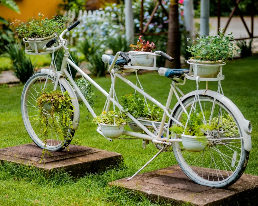 Upcycled white bicycle transformed into a planter overflowing with colorful flowers and greenery.