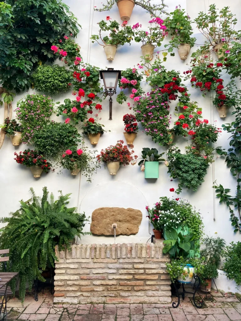 Lush vertical garden with various houseplants cascading down a wall with a decorative fountain nearby.